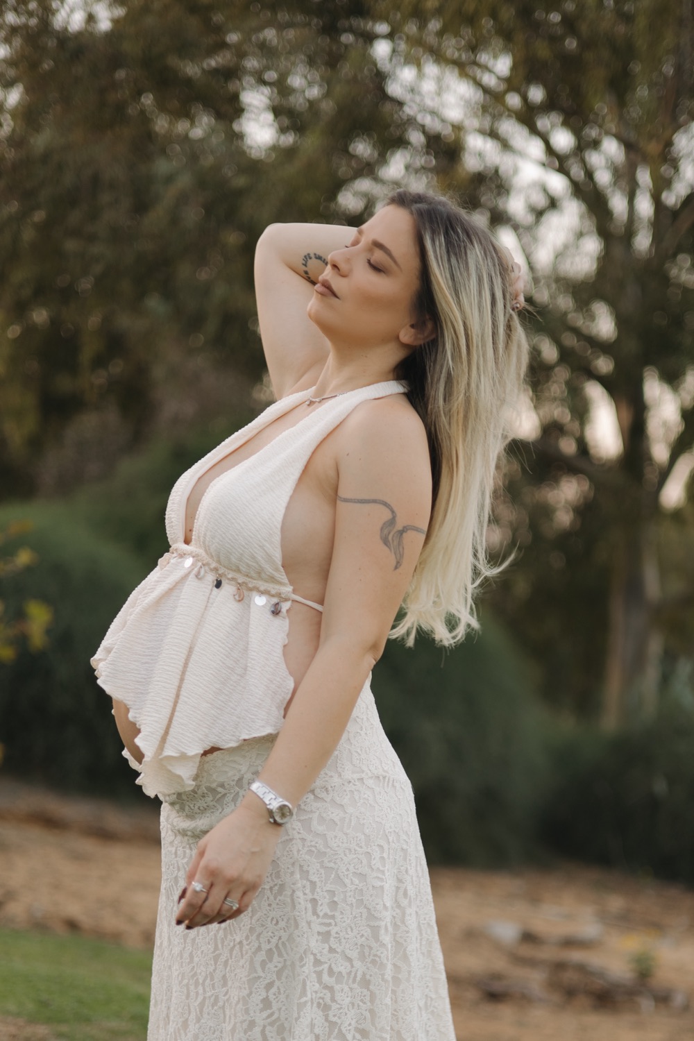 אישה בהריון בשמלה לבנה בשקיעה, יד בשיער